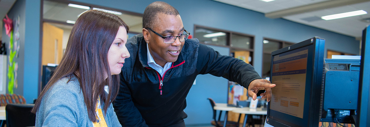 A UW Oshkosh advisor points out information on a computer screen while assisting a student in the advising office.