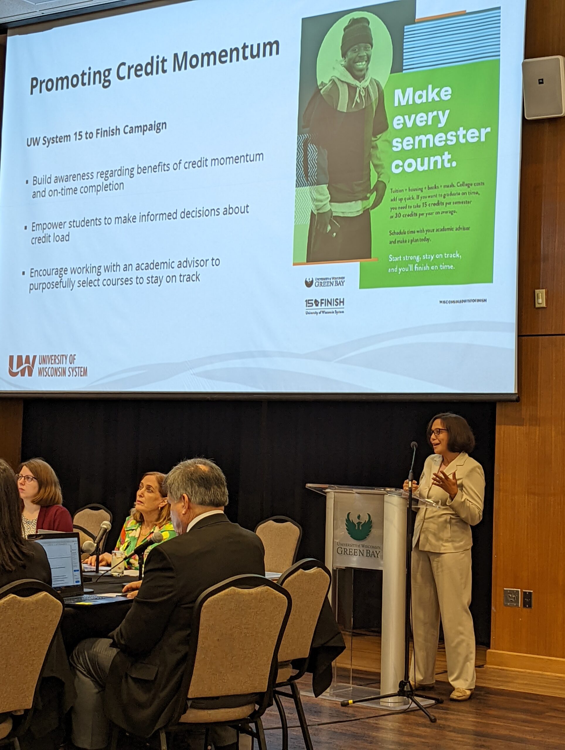 Angela Kellogg at podium with PowerPoint slide about credit momentum in the background at a UW System Board of Regents presentation on advising in August 2022.