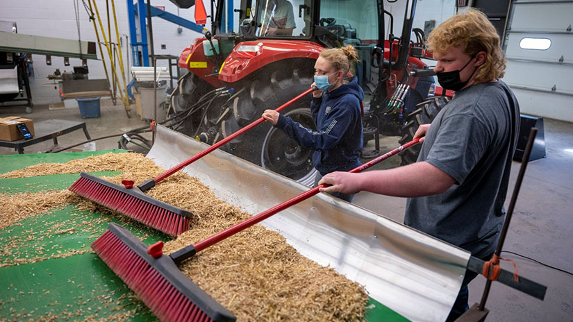 Photo of students Rames Frisch, in tractor, Alex Pierson and Kyle Leis conducting research to determine how to improve a 1960s combine’s performance.