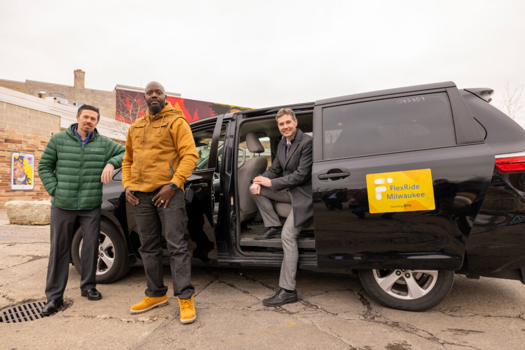 Photo of Eric Lynde (from left) of the Southeastern Wisconsin Regional Planning Commission and UWM Professor Robert Schneider (right) meeting FlexRide driver Mitchell Smith at the Sherman Phoenix pickup location. It is one pickup site for a ride to employers in Butler and Menomonee Falls. (UWM Photo/Troye Fox)