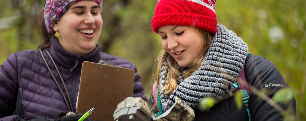 Photo of UW-Whitewater Assistant Professor Andrea Romero, left, and biology student Noel Schmitz reacting as the counter on a motion detecting trail camera indicates some 3,000 images, but they know many will be wind-blown debris and perhaps a few joggers. They were collecting trail cameras on the campus nature preserve on Nov. 1, 2019, to contribute wildlife images to the Smithsonian Snapshot USA project. (Photo by Craig Schreiner/UW-Whitewater)