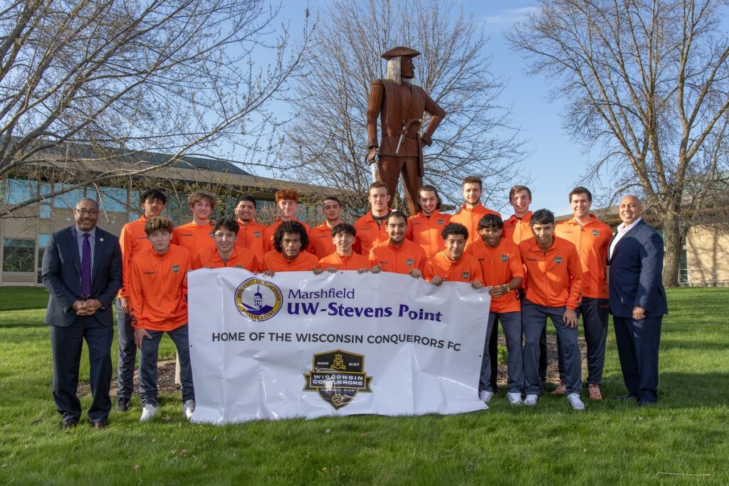 Photo of members of the Conquerors Football Club pictured at the UWSP at Marshfield campus with Chancellor Thomas Gibson (left) and Campus Executive Tony Andrews (right).