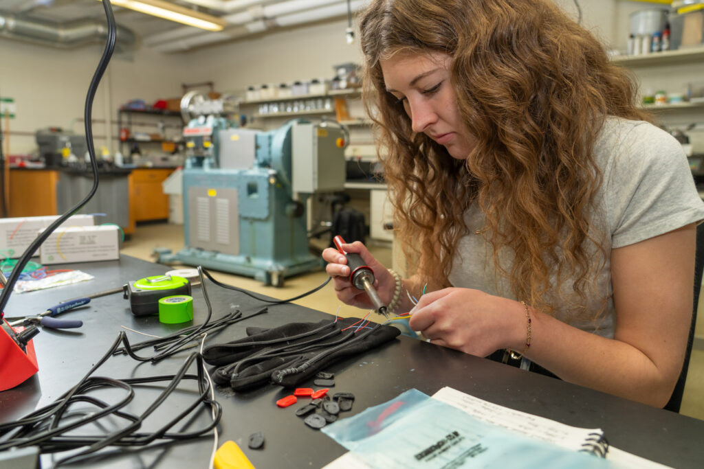 Photo of UW-Eau Claire senior Maddie Mousel working on a portable vibrating glove with the potential to reduce tremors in Parkinson’s disease patients. This interdisciplinary Blugold research project recently received key financial support thanks to an agreement between UW-Eau Claire and Mayo Clinic Health System. (Photo credit: UW-Eau Claire)