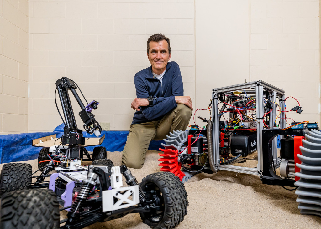 Photo of mechanical engineering professor Dan Negrut posing with a space rover used for testing. (Photo by Joel Hallberg)