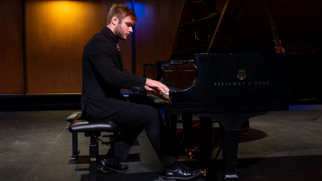 Photo of Ethan Squires rehearsing at the piano before a recital in Brodbeck Concert Hall.