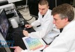 scientists in lab coats looking at a computer screen
