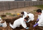 students in lab coats digging a hole