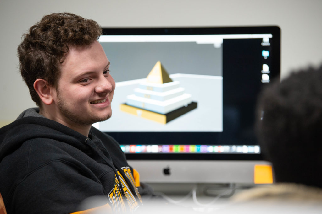 Photo of an art student in a digital fabrication class, who recently gained real-world professional experience working with one of the community's most prestigious employers, Oshkosh Defense. 