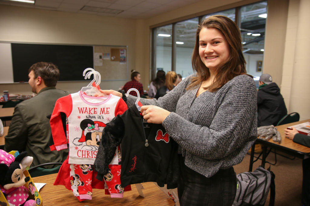 Photo of a UW-Superior student-athlete holding up children's clothes for the university's Giving Tree