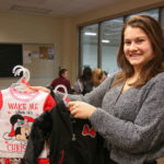 Photo of a UW-Superior student-athlete holding up children's clothes for the university's Giving Tree