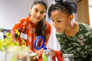 Photo of Amelia Pearson (right) listening to Olympia Mathiaparanam, research specialist at the Wisconsin Center for Education Research, at a Lakeshore Nature Preserve education table during a UW-Madison South Madison Community Partnership event held in Villager Mall on Park Street on Sept. 12, 2019. The event provided community members from the Southside Madison neighborhood the opportunity to meet with various program representatives from UW-Madison and enjoy a meal together. (Photo by Bryce Richter/UW-Madison)