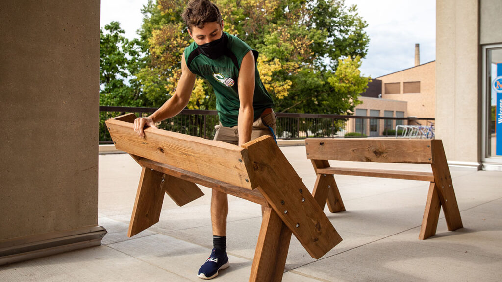 Photo of UW-Platteville student volunteer carrying a bench to set up an outdoor classroom during the COVID-19 pandemic