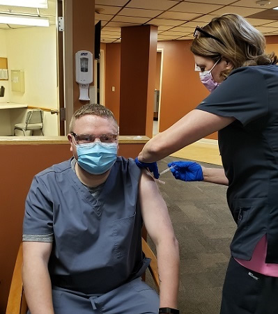 Photo of Adam Hartz, receiving the first dose of the COVID-19 vaccine at the clinic where he works,