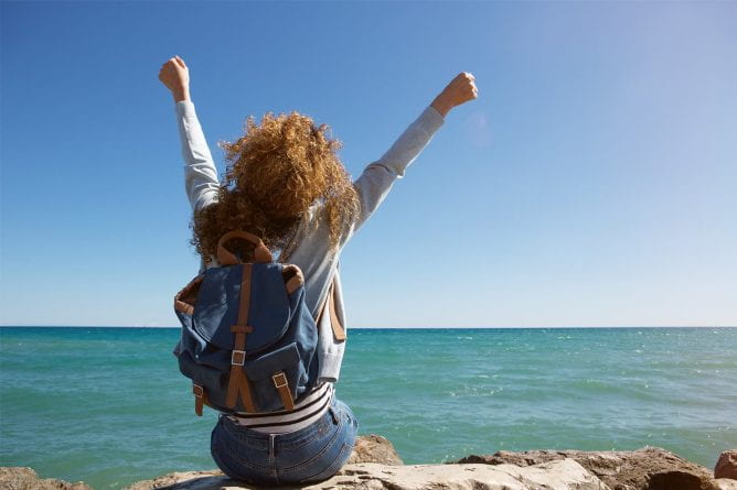 Photo of student sitting on shore with arms raised