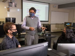 Photo of Dr. Rahul Gomes (center), an assistant professor of computer science at UW-Eau Claire, talking with his student researchers Aaron Huber (left) and Avi Devy Mohan (right) about a collaborative project they are working on with Mayo Clinic Health System.