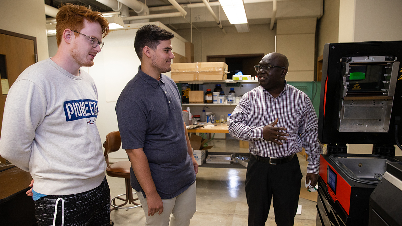 Photo of Dr. John Obielodan explaining the workings of a newly acquired selective laser sintering machine to some of his students in the lab. The machine was purchased through a Dairy Innovation Hub Supplies and Equipment grant.