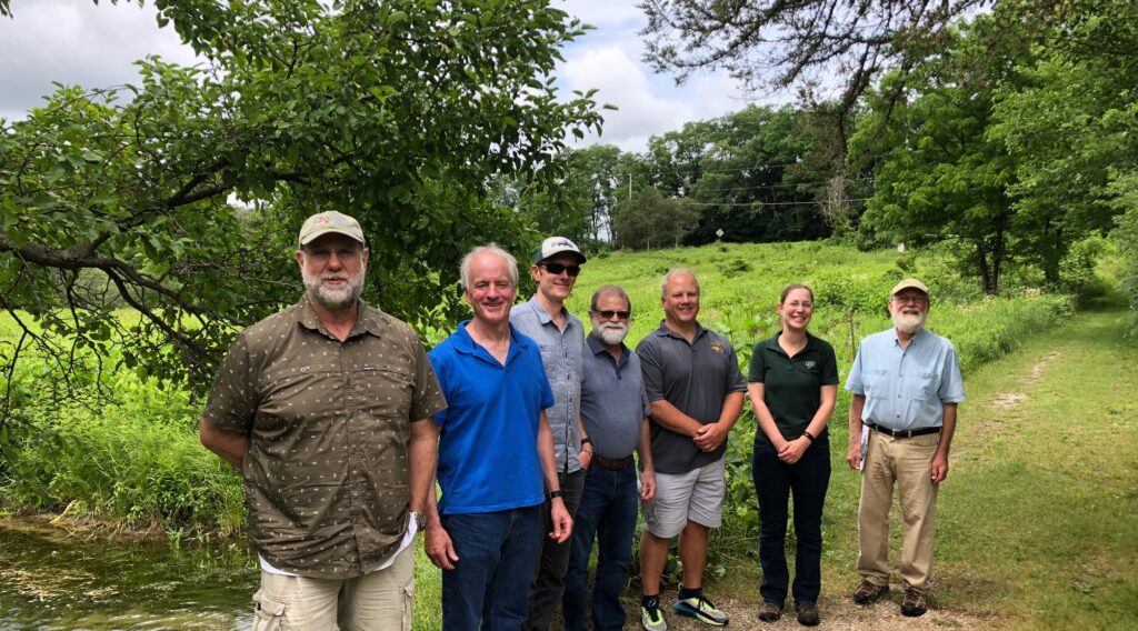Photo of faculty from five UW campuses who met in July at the UW-Waukesha field station for a daylong retreat to plan Freshwater Science 101, a new course to be offered to students at UW-Madison, UW-Milwaukee, UW-La Crosse, UW Oshkosh, and UW-Parkside. Pictured are Eric Strauss, Robert Stelzer, Jake VanderZanden, Mike Carvan, Greg Kleinheinz, Jessica Orlofske, and Marlin, who gave them a tour of the station. Taking the photo was Tracy Boyer. Photo courtesy of Heidi Jeter.