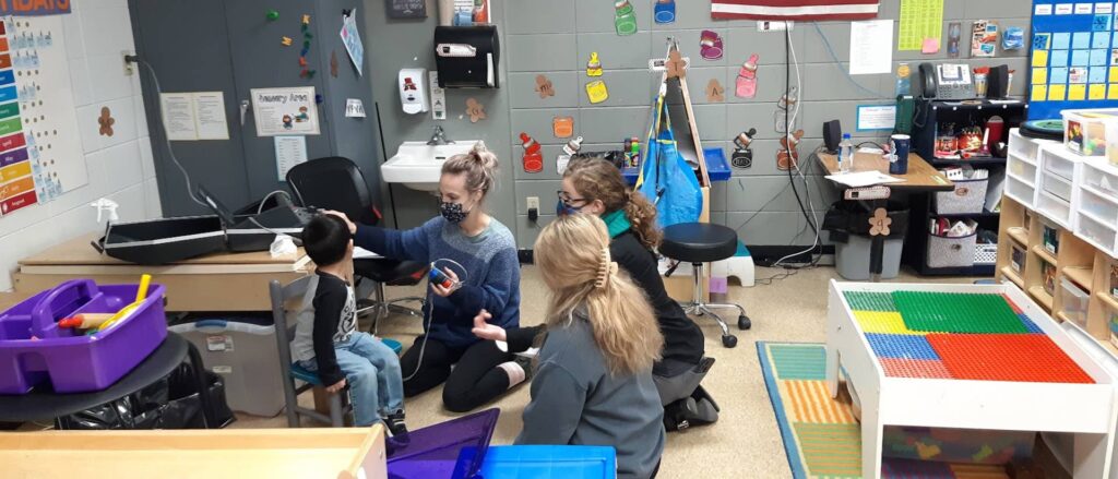 Photo of Carissa Phelps, a CSD second-year graduate student, Hope Wachholz, an undergraduate Spanish interpreter, and Arcadia Childcare Center director Jolynn Bourland working together to complete a young boy’s hearing screening. (Submitted photo)