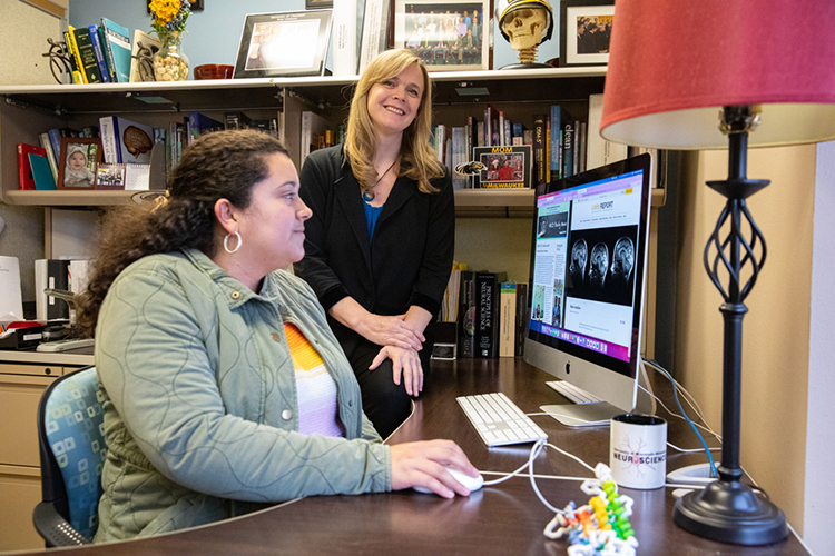 Photo of Krista Lisdahl (standing), professor of psychology, and graduate student Ashley Stinson looking at brain scans of adolescents participating in the ABCD Study, the largest long-term study of brain development and child health in the United States. (UWM Photo/Troye Fox)