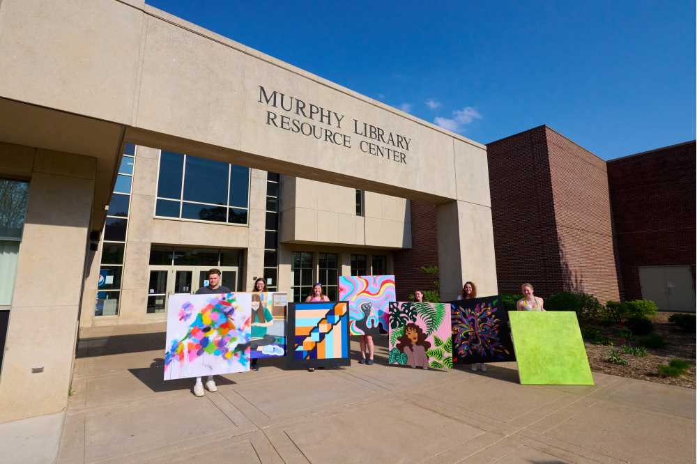 Photo of the students and their work, which included, from left, Greg Voves, Katie Erdahl, Cassidy Hermann, Kenzie O’Shea holding work of Mattie Blanck, Mattie Blanck, Emma Waller and Gretchen Fischer. Voves, who took a mixed media approach using acrylic, oil, and spray paint, says his work "serves as an escape from an environment that is so heavily rooted in facts and offers viewers something to interpret for themselves. After extensive research in color psychology, I decided to implement a wide range of hues and tones that can determine subconscious emotions or behavior." Blanck says her painting “The Spread of Creativity," creates a serene atmosphere that eases anxiety and gives a peaceful place to work or read. “Plants represent new growth,” she explains, “which can be motivating for those who utilize the library to seize opportunities to grow and expand their knowledge." Blanck's second painting accepted was titled, “Library Garden."