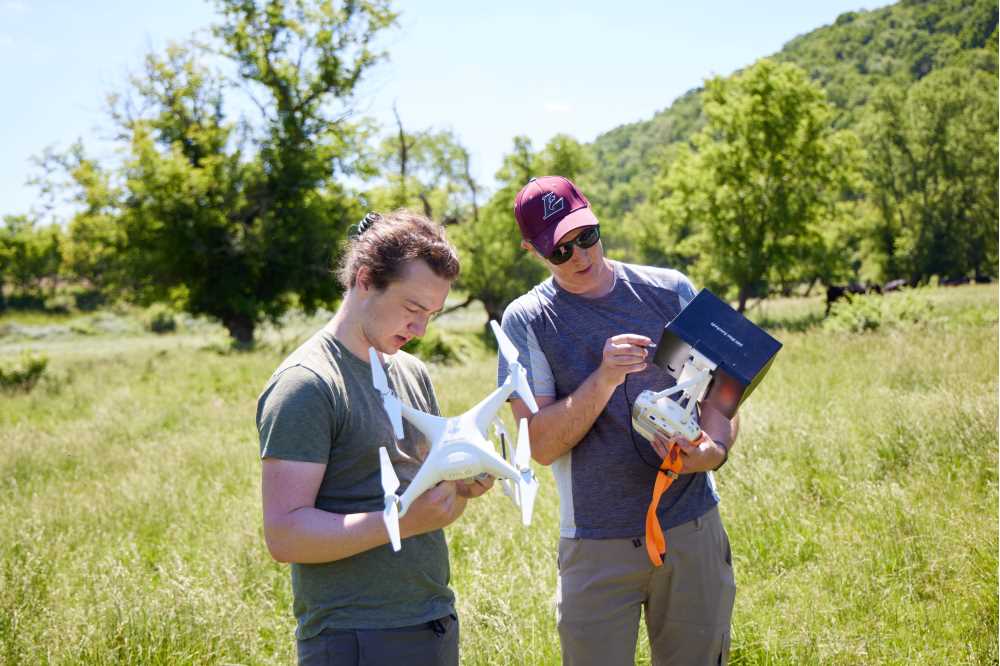 Photo of UWL student Travis Key (left) and UWL Professor Colin Belby preparing to fly a drone over a two-mile stretch of Plum Creek in rural Crawford County. The team is using drone imagery, soil samples and geographic information to help the Mississippi Valley Conservancy restore the area to its natural state.