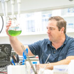 Photo of Todd Miller working with a beaker that contains Nostoc, a cyanobacteria isolated from Lake Superior that produces a novel neurotoxin. (UWM Photo/Troye Fox)