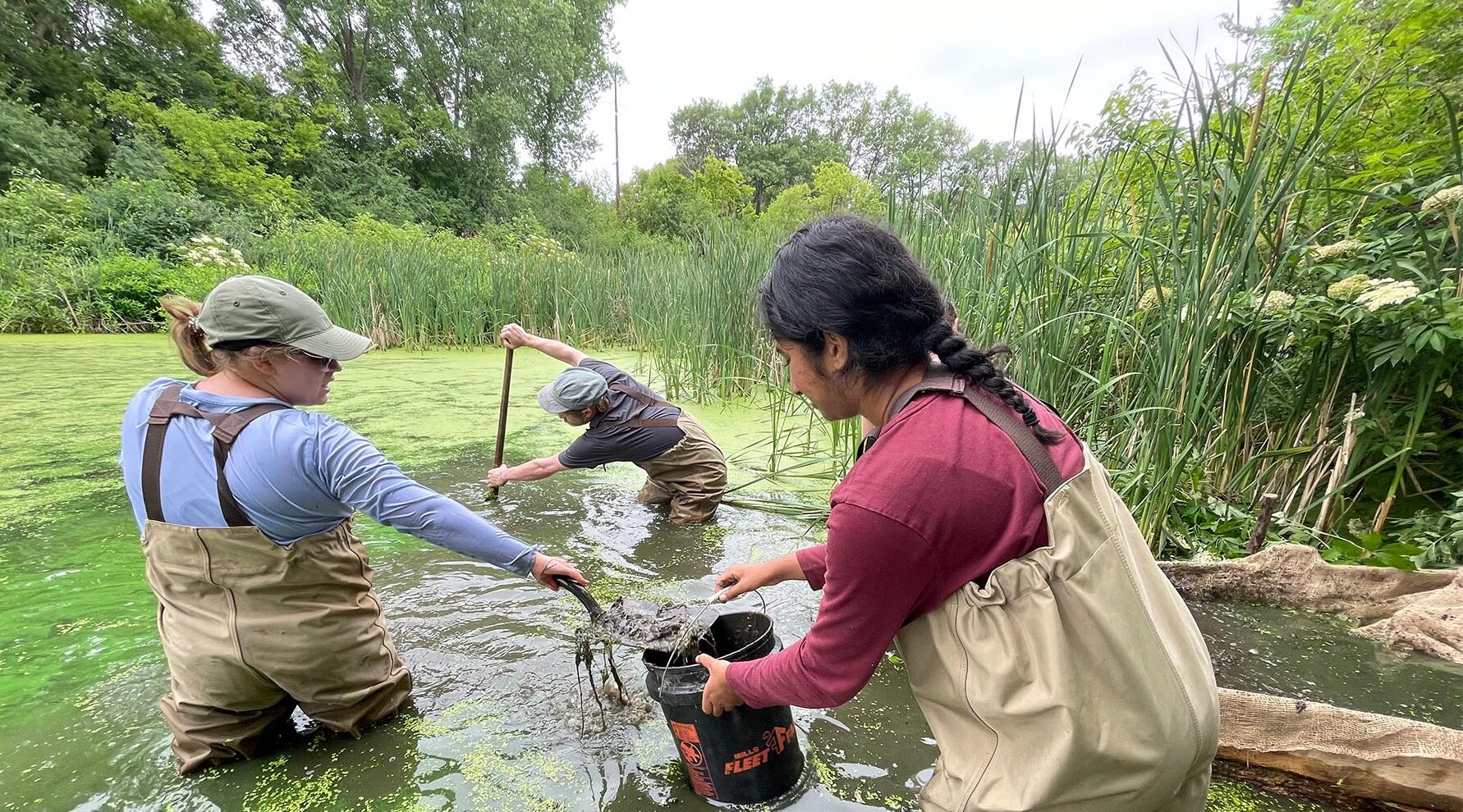 Photo of scooping soil samples from the riverbed with Senior Lecturer Arthur Kneeland (center back) with LAKES students Evelyn Dyer (left) and Sahi Chundu.