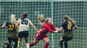 Photo of Elaina LaMacchia (in red) making a save during a UWM match. LaMacchia led the nation in goals-against average in 2021. (Milwaukee Athletics photo)