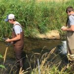 Photo of Kal Breeden, left, and Dylan Kostuch wading through a stream in Dunn County as part of the water monitoring program. / UW-Stout
