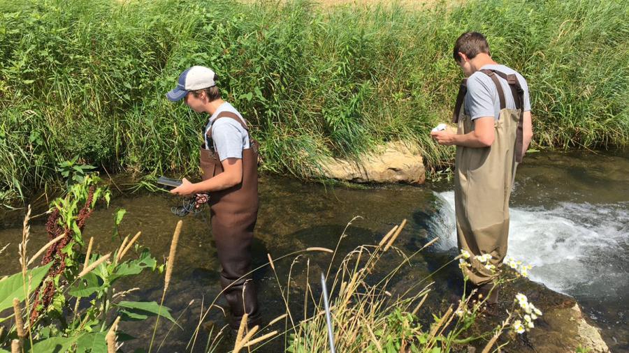 Photo of Kal Breeden, left, and Dylan Kostuch wading through a stream in Dunn County as part of the water monitoring program. / UW-Stout