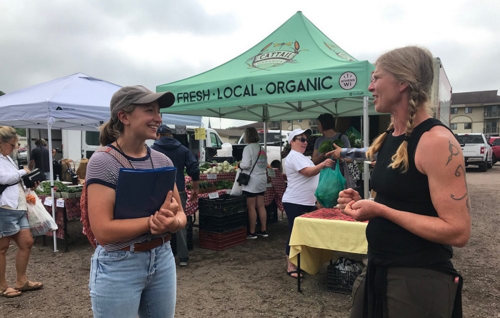Photo of alumna Taylor Christiansen (left), regional farmers market coordinator, who is among collaborators aiming to increase access to local food and strengthen markets through community partnerships. Here, she speaks with farmer Kat Becker of Cattail Organics at the Wausau Farmer’s Market.