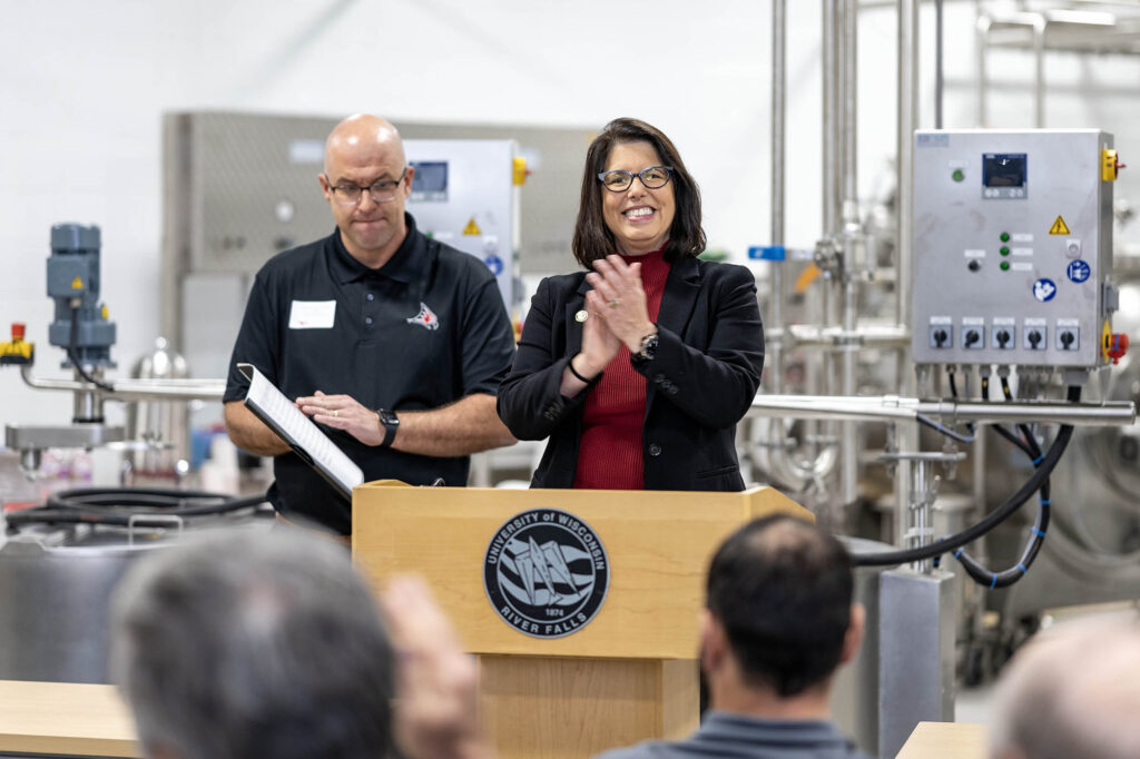 Photo of Chancellor Maria Gallo sharing applause with Trevor Wuethrich, Grassland Dairy Products, Inc. president, during a special gathering Thursday morning in the UWRF Dairy Pilot Plant.