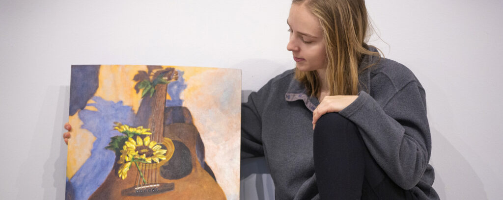 Photo of Emma Siskoff, an art major from New Berlin, shown with her painting, “Comforts of My Home,” a composition including her 94-year-old grandmother’s guitar and sunflowers, on Thursday, Dec. 8, 2022. (UW-Whitewater photo/Craig Schreiner)