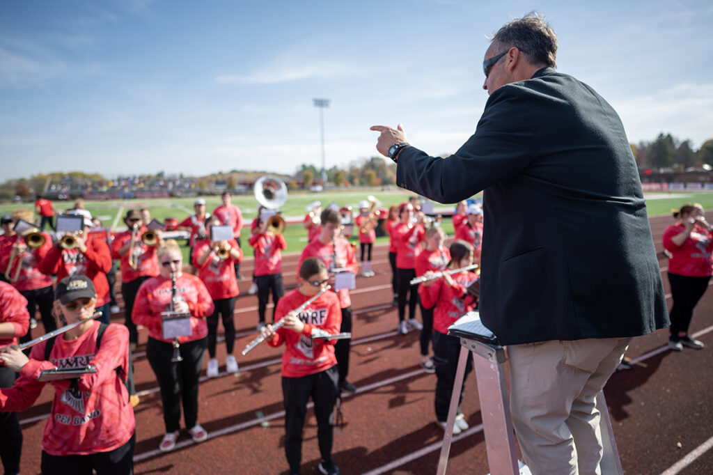 Photo of Tom Barnett, UW-River Falls marching band director, leading the UWRF pep band at Smith Stadium at Ramer Field in October 2022 prior to the start of a home game against UW-Eau Claire. 