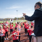 Photo of Tom Barnett, UW-River Falls marching band director, leading the UWRF pep band at Smith Stadium at Ramer Field in October 2022 prior to the start of a home game against UW-Eau Claire.