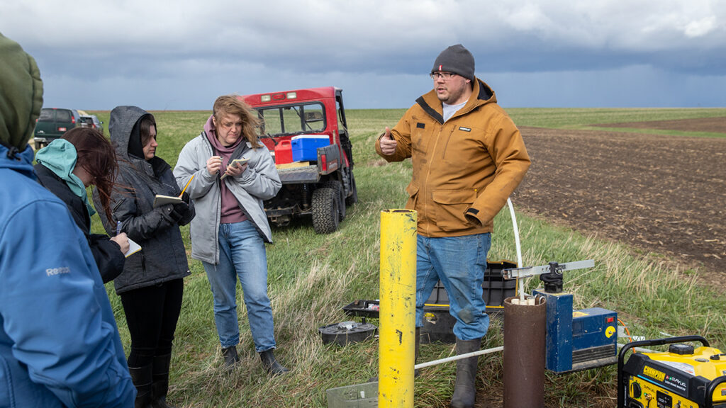 Photo of students learning about the groundwater sampling network at Pioneer Farm and receive a demonstration on how to sample water from wells.