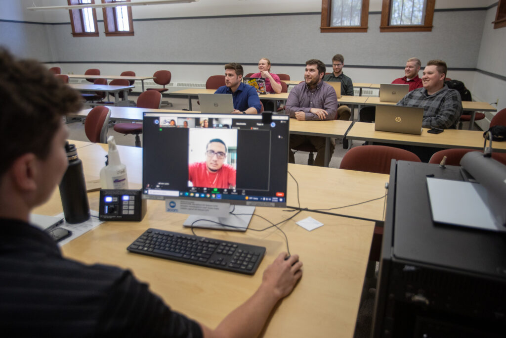 Photo of student teams, who were paired with clients in Honduras, giving them the unique opportunity to help under-resourced entrepreneurs, while navigating a different language and culture. Pictured in back row: Evan Benkovich, Bryant Keeffer, and Nick Schaal; middle row: Darian Wright, John Biernat, and Alex Schulz; and in front at the desk: Joshua Ellsoos. (Photo credit: UW-Platteville)