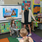 Photo of Halle Nicolet and Marli Felicijan, both senior Spanish education majors, shown here leading a class of young students through a lesson about spending a day in Valencia, Spain. At the end of the seven classes, the elementary school students presented the topic in Spanish to visiting parents.