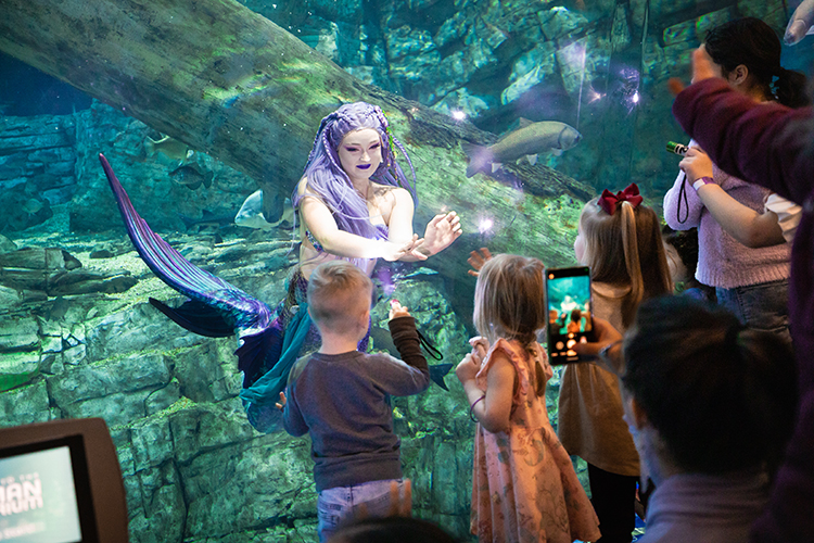 Photo of Pierce VanValkenburg as Mermaid Echo interacting with children attending an educational performance at Discovery World. (UWM Photo/Elora Hennessey)