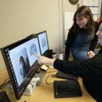 Photo of Psychology Professor Christine Larson and undergrad Alexandra Lato examining a brain scan on the computer. Telltale signs of trauma can be seen in brain scans of people who have visited the emergency department. "We've probably scanned over 1,000 people at MCW over the years," Larson said. "It still feels like a privilege to see what's happening inside people’s brains." (UWM Photo/Elora Hennessey)