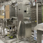 Photo of a worker helping finish moving a new pasteurizer into the dairy pilot plant at UW-River Falls. The new equipment is a key part of the remodeled Wuethrich Family/Grassland Dairy Center of Excellence that could open as soon as this fall. UWRF photo.