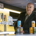 Photo of Stanislav Dobrev, professor of organizations and strategic management in the UWM Lubar College of Business, showing some examples of craft beer names. Positive names include Sunny Little Thing and Happy Place. More negative or quirky names are Voodoo Ranger and Deadhead. The latter duo had better online reviews, according to Dobrev's study, because they were perceived as more authentic. (UWM Photo/Troye Fox)