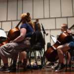 Photo of Professor Benjamin Whitcomb, left, taking an athlete’s stance as he coaches camp musicians. Strings Camp students work to refine their music for a performance in Young Auditorium on the UW-Whitewater campus. (UW-Whitewater photo/Craig Schreiner)