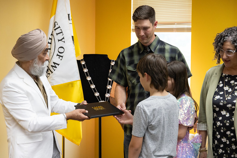Photo: UW-Oshkosh Chancellor Manohar Singh hands a diploma to Barry Moodie, as his children Emmett and Kate and his late wife’s mother, Mary Altenburg, look on.