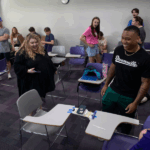 Photo: Students in Communication 328: Managing Conflict, a class taught by Assistant Professor Courtney Powers that is part of the Health and Leadership Studies curriculum, worked on a team-building classroom exercise on Tuesday, Sept. 17, 2024, using paper, string, tape and lengths of dried spaghetti to devise and build bridges to support weight placed on them. Powers, center, and entrepreneurship major Nazier Jones, right, react as his team's bridge between two desktops sustains a cell phone and deck of cards. (UW-Whitewater photo/Craig Schreiner)