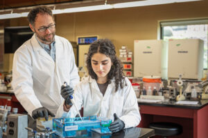Photo of Troy Skwor, associate professor of biomedical sciences, working with undergraduate researcher Yara Haddad in his lab. The research aims to pinpoint antibiotic-resistant genes in drug-resistant bacteria. (UWM Photo/Andy Manis)