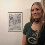 Photo of UW-Platteville alumna Trinity Schlorf with her piece of art hanging at Lambeau Field