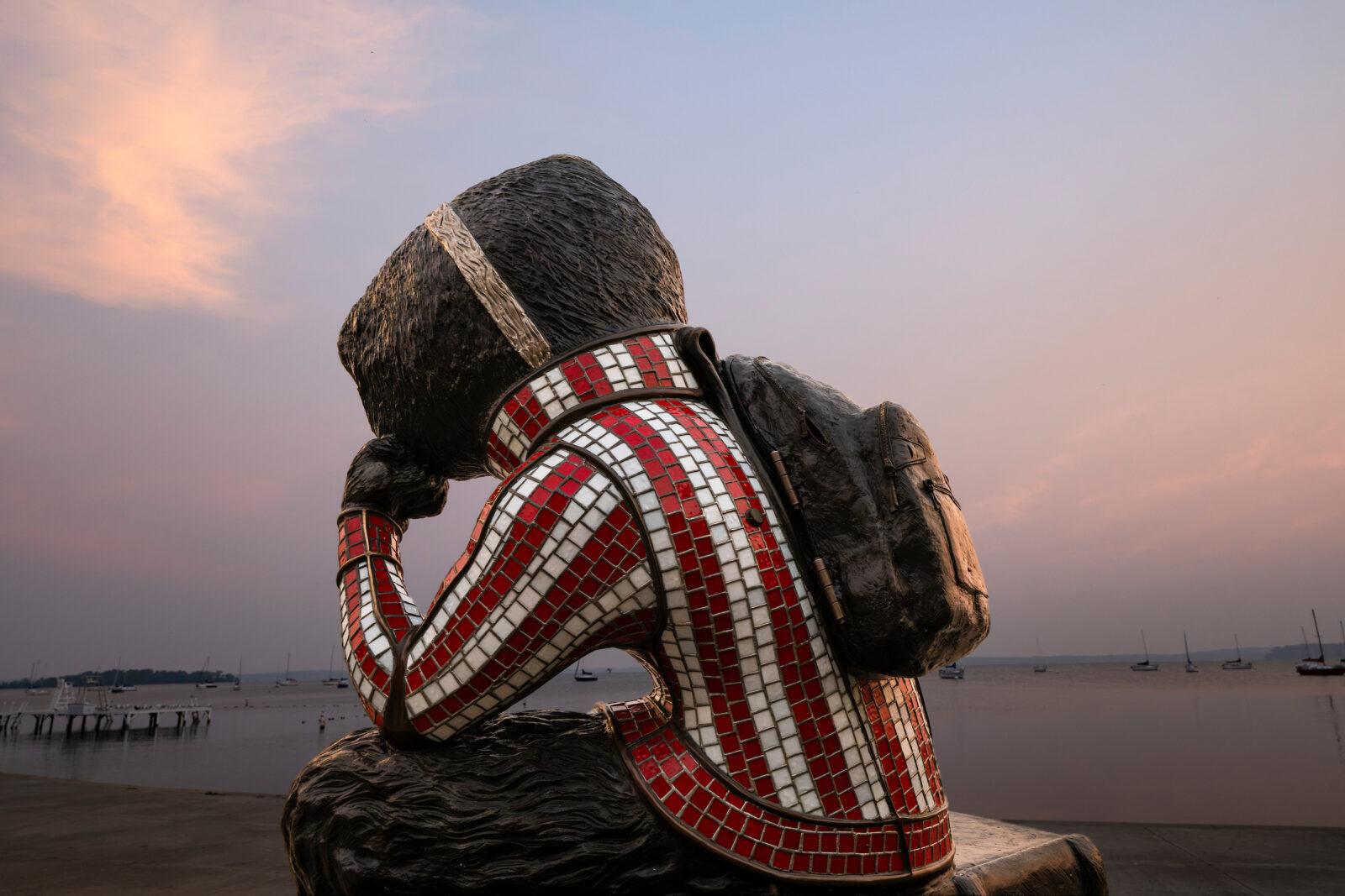 Photo: “Well Red,” a sculpture by artist Douwe Blumberg of UW-Madison mascot Bucky Badger, looks onto a wildfire smoke muted summer sunrise as it paints Lake Mendota in pastels near Alumni Park at the University of Wisconsin–Madison on July 20, 2026. Photo: Taylor Wolfram / UW–Madison.