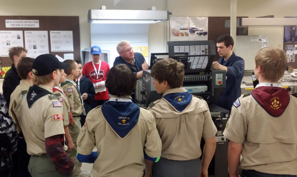 UW-Stout printing lab specialist Chad Nyseth, back left, and UW-Stout student Nick Egan demonstrate the use of a printing press to Boy Scouts during a merit badge class on campus.