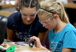 A high school lab assistant, left, watches as a STEPs for Girls participant wires a battery harness for her robot. To make the harness, girls cut, stripped and soldered the wires.